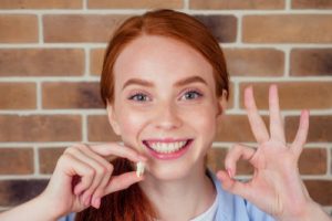 redhaired ginger female with snow-white smile holding white wisdom tooth after surgery removal of a tooth